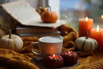 Cup of coffee and burning pumpkin shaped candles on soft sweater. Autumn atmosphere