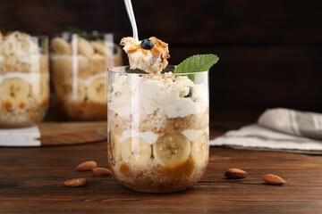 Taking tasty trifle dessert at wooden table, closeup
