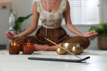 Young woman practicing yoga on floor indoors, focus on smoldering incense stick