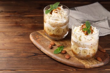 Tasty trifle dessert. Sponge cake, banana and whipped cream in glasses on wooden table