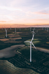 Modern windmills with rotating propellers standing in rural farmland agri meadow over orange sunset...