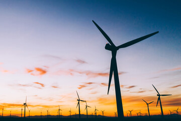 Silhouette of windmills station with propellers generating alternative clean green power from eco...