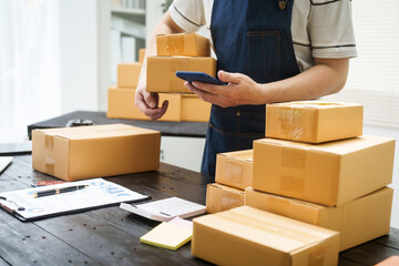 Fototapeta premium A man is working at his desk, preparing parcel boxes for shipment. He checks and packs items carefully, using shockproof materials, and attaches labels before sending them to customers via EMS.