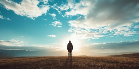 A silhouette on a field gazes towards a magnificent sunrise, capturing the spirit of solitude and open adventure.