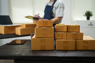 Fototapeta premium A man is working at his desk, preparing parcel boxes for shipment. He checks and packs items carefully, using shockproof materials, and attaches labels before sending them to customers via EMS.