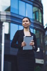 Fototapeta premium Cheerful caucasian business woman in stylish skirt suit enjoying time for messaging via modern digital tablet using high speed 4g internet in roaming for making business deals in offline mode