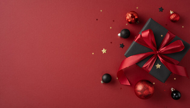 A beautifully wrapped black gift box with a red ribbon surrounded by red and black ornaments and stars on a festive red backdrop