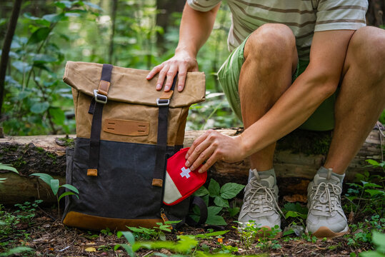 Man placing a first aid kit into his hiking backpack while resting in a forest, preparing for outdoor adventure.