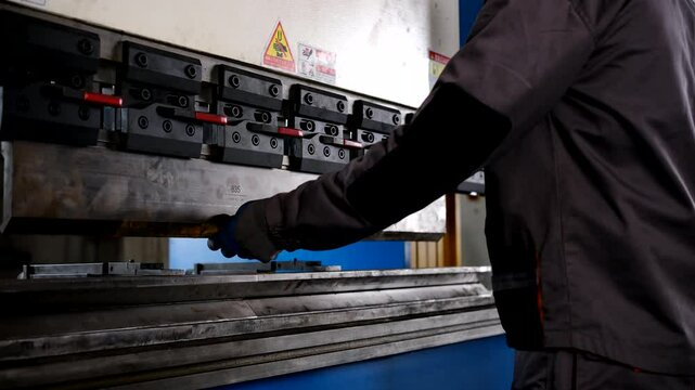 Man working with sheet metal on CNC hydraulic press brake. He puts the part and bends it into a large machine at an angle