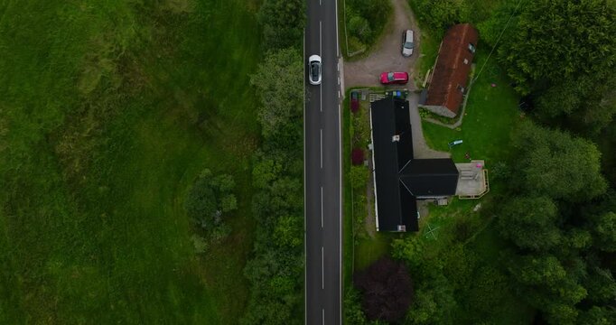 Beautiful view from above of electro car moving past modern houses and bright green fields in Scotland
