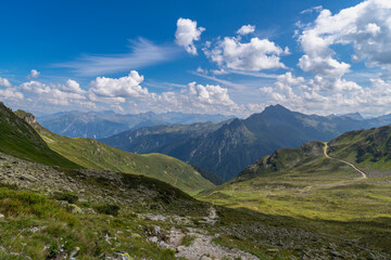 panoramic view over steep Swiss mountains, border with stony rocky mountain with alpine meadows and gravel fields, hikers path way through pasture and boulders up to the summit, holiday destination