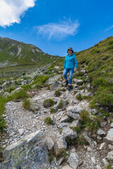 Woman on the way through beautiful mountain meadows with alpine autumnal flowers. the hiker on the footpath climbs the stony path up to the summit. beautiful alpine landscape with view over Austria