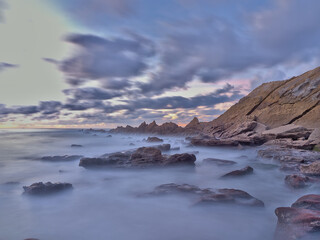 Atardecer en el mar con las rocas en primer plano y un cielo con nubes