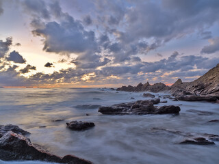 Atardecer en el mar con las rocas en primer plano y un cielo con nubes