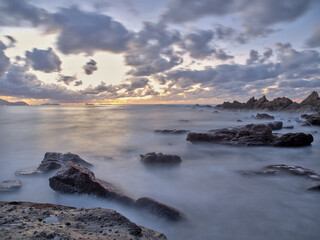Atardecer en el mar con las rocas en primer plano y un cielo con nubes