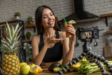 Young woman recording video on tripod mounted camera in kitchen for her healthy food vlog