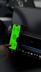 In a car interior, likely driven by a taxi or rideshare driver, a hand touches a smartphone with a green mockup screen mounted on the dashboard