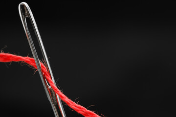 Sewing needle with red thread on black background, closeup. Space for text