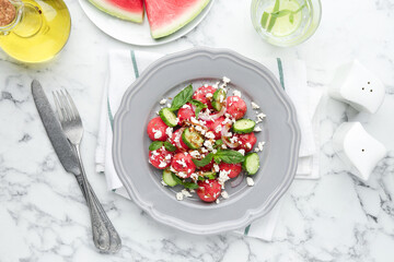 Delicious watermelon salad with feta cheese, vegetables and spices served on white marble table, flat lay
