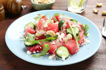 Tasty salad with watermelon, feta cheese, cashews and arugula on wooden table