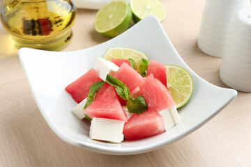 Tasty salad with watermelon, feta cheese, lime and mint on wooden table