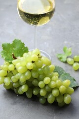 Fresh ripe grapes and glass of wine on grey table
