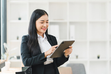 professional woman in black suit smiles while using tablet in modern office setting. bright environment enhances her positive demeanor and focus on work.