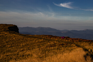 purple tent on the side of a trail on the edge of a mountain range at sunset, when everything around is bathed in light