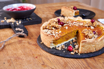 Top view of pumpkin pie with pecans and cranberries lying on a black dish on a black wooden tray