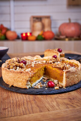 Top view of pumpkin pie with pecans and cranberries lying on a black dish on a black wooden tray