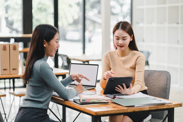 Two women engaged in collaborative discussion at modern workspace, sharing ideas while using tablet and laptop. Their interaction reflects teamwork and creativity.