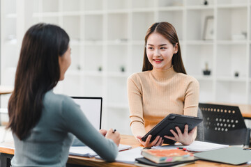 Obraz premium Engaged conversation between two women in modern office setting, one holding tablet and other taking notes. atmosphere is collaborative and professional.