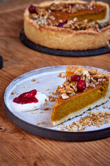 A slice of pumpkin pie with cream and cranberries rests on a ceramic plate on a wooden table