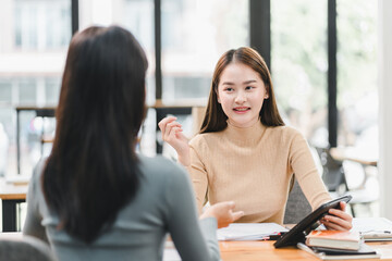 Engaged conversation between two women in modern office setting, showcasing collaboration and communication. atmosphere is professional and friendly, highlighting teamwork and discussion.