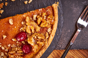 Top view of pumpkin pie with pecans and cranberries lying on a black dish on a black wooden tray