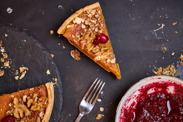 Top view of pumpkin pie with pecans and cranberries lying on a black dish on a black wooden tray