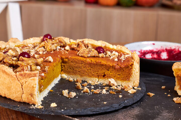 pumpkin pie decorated with nuts and cranberries stands on a black stand on a wooden table side view