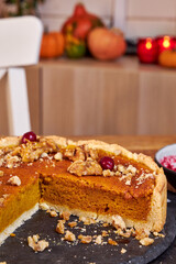 pumpkin pie decorated with nuts and cranberries stands on a black stand on a wooden table side view