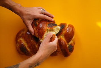 Hands take part of challah bread on yellow background
