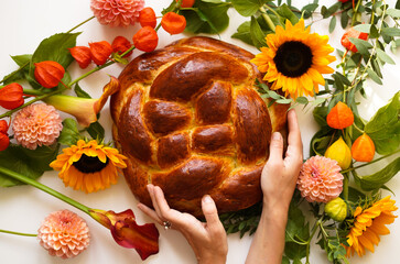 fresh homemade bread baked for the holiday - round challah in hands on a bright background with flowers