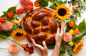 Top view, female hands holding round fresh challah, on Rosh Ha Shana with fresh flowers background. Jewish New Year. Traditional home baking for the holiday