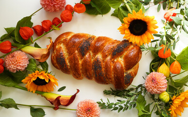 Close-up of challah decorated with poppy seeds against a background of pale beautiful flowers. Shabbat meeting with homemade bread