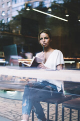 Pondering female writer thinking about information for new chapter in book sitting with notebook and laptop computer in cafeteria, pensive woman thoughtful looking away while planning organisation