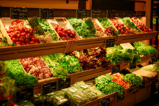 Fresh vegetables displayed in neat rows on shelves at a grocery store, showcasing a variety of greens and tomatoes under warm lighting.