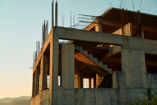 Sunset light casting warm hues on an unfinished concrete building with exposed steel rebar.