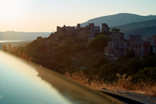 Early morning light bathes an abandoned stone village with a backdrop of rolling hills and a calm lake.