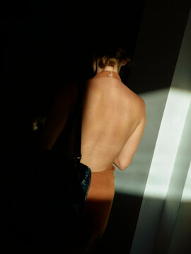 Bare back of a woman standing in dim light with a shadow pattern across her skin.