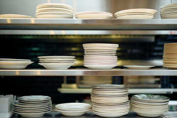 Stacks of various white ceramic plates on metal shelves in a commercial kitchen.