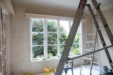 Renovation in progress inside a room with an open window overlooking a garden, featuring a ladder, tools, and unpainted walls, Auckland, New Zealand