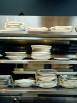 Stacks of white plates organized on metal shelving in a professional kitchen.